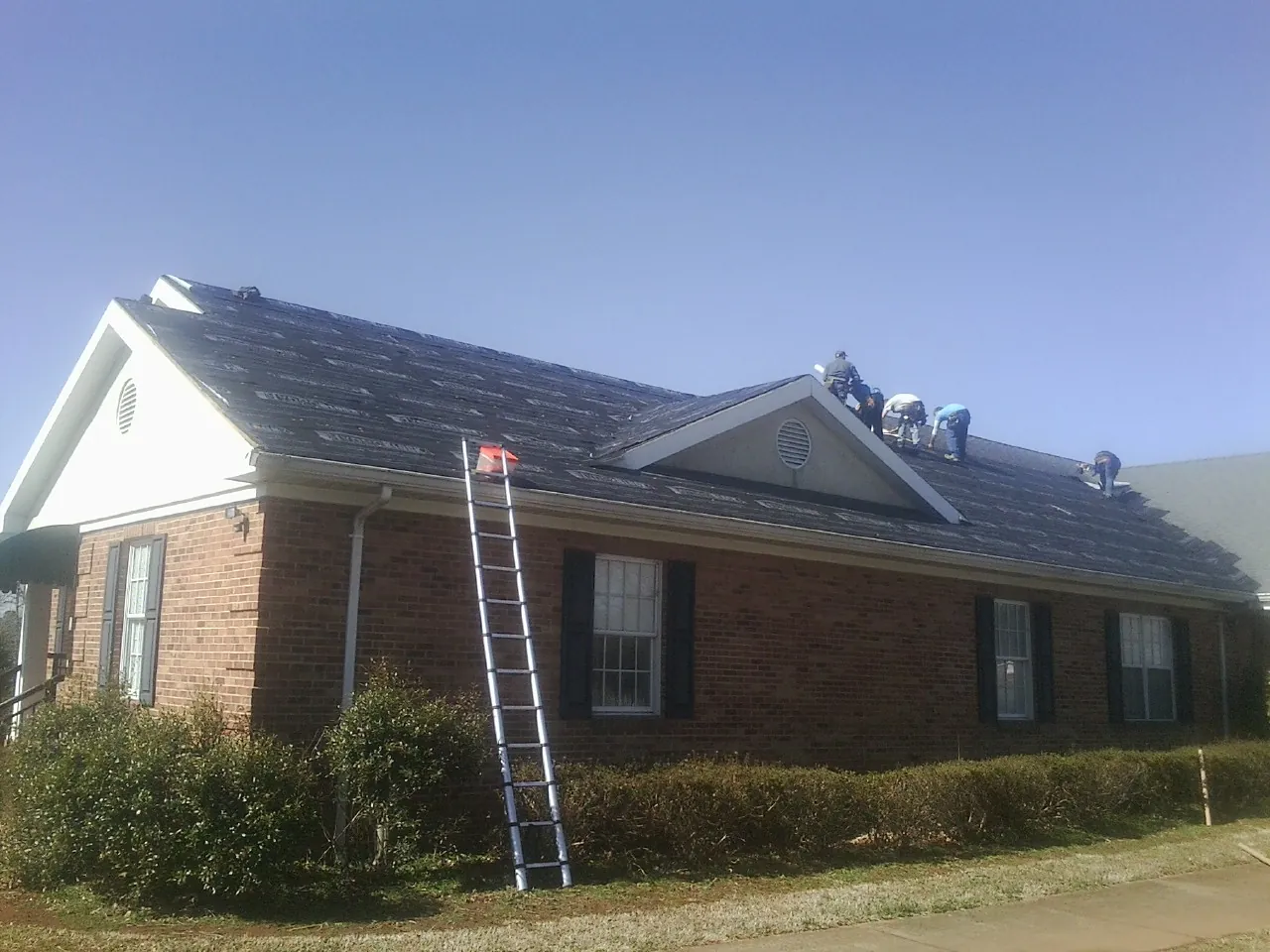 Crew tearing shingles off a brick ranch roof with a ladder set — Emergency Roof Repair work by our crew in Pomaria