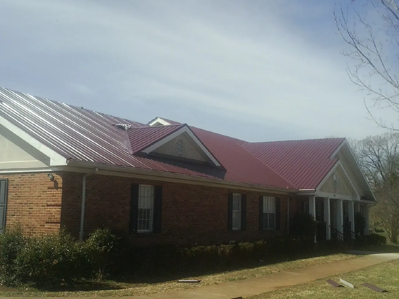 Red metal roof with gabled entries on a long brick building, from a Hail Damage Roof Repair job in Pomaria