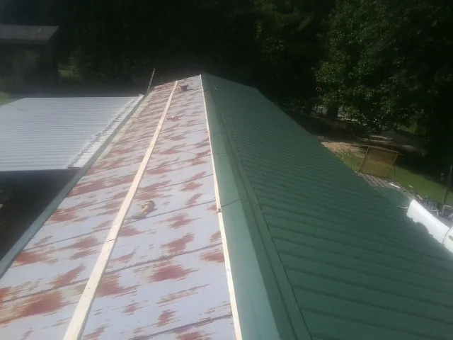 Old rusted panels beside newly installed green metal roofing — Wind Damage Roof Repair by Roofing Brothers in Pomaria