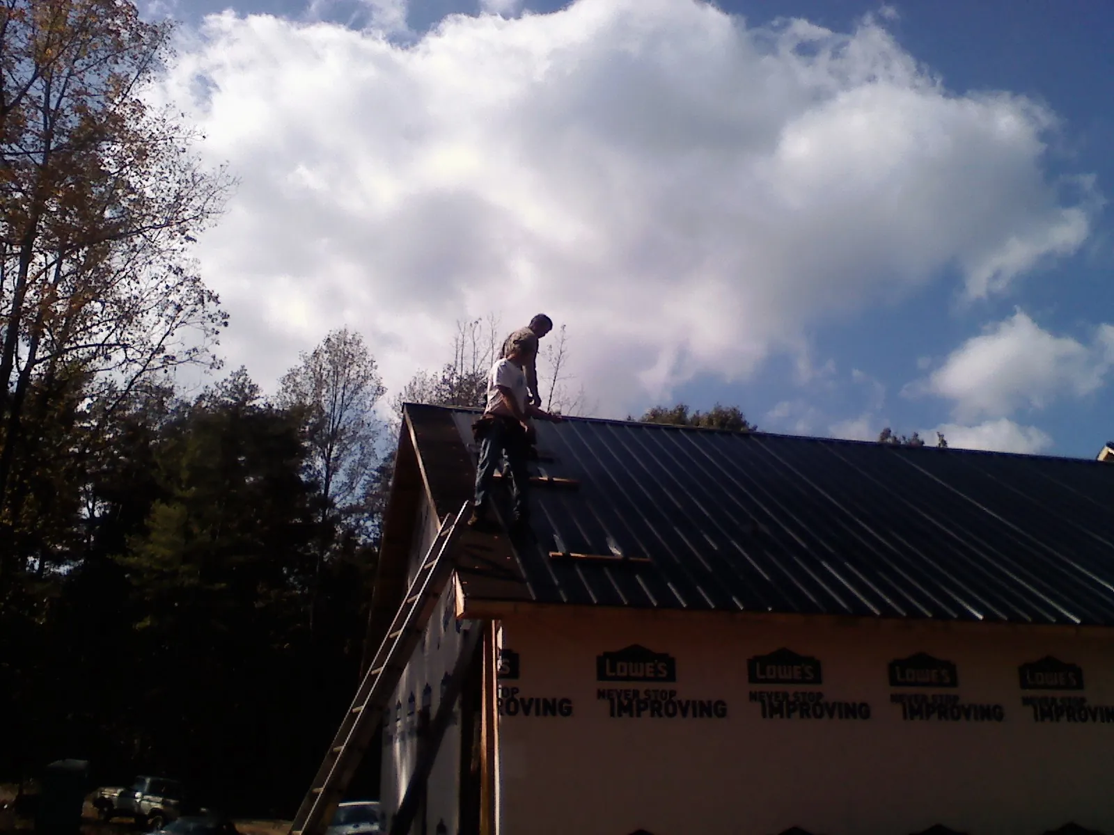 Roofer fastening dark metal panels high against a cloudy sky, from a Roof Inspection job in Pomaria