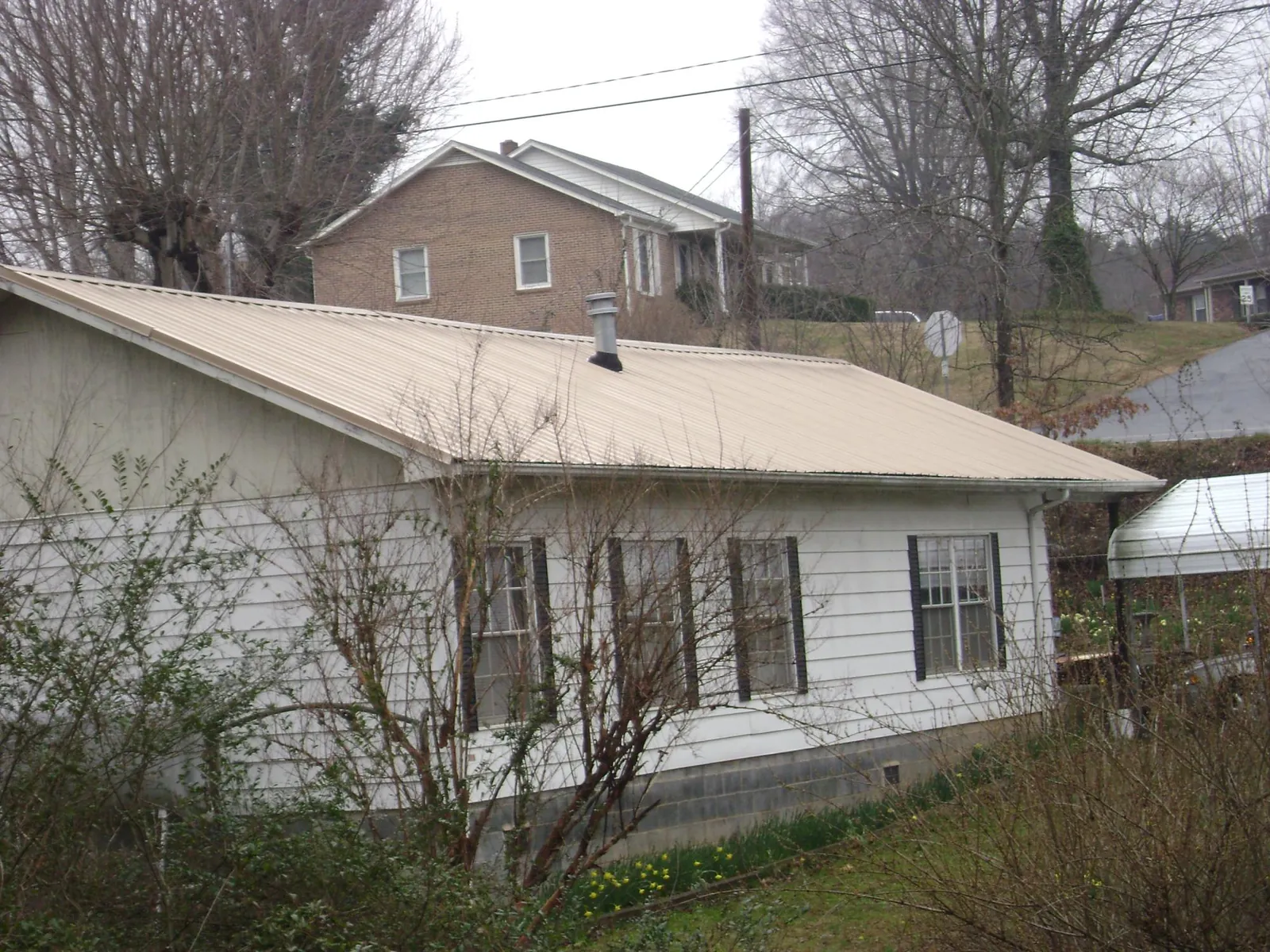 Tan metal roof on a white sided house set into a hillside — Commercial Roofing by Roofing Brothers in Pomaria